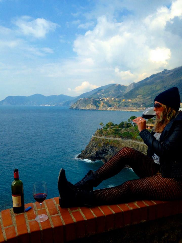 Me, a young woman, sitting on top of an overlook in Cinque Terre, Italy, drinking a glass a red wine.