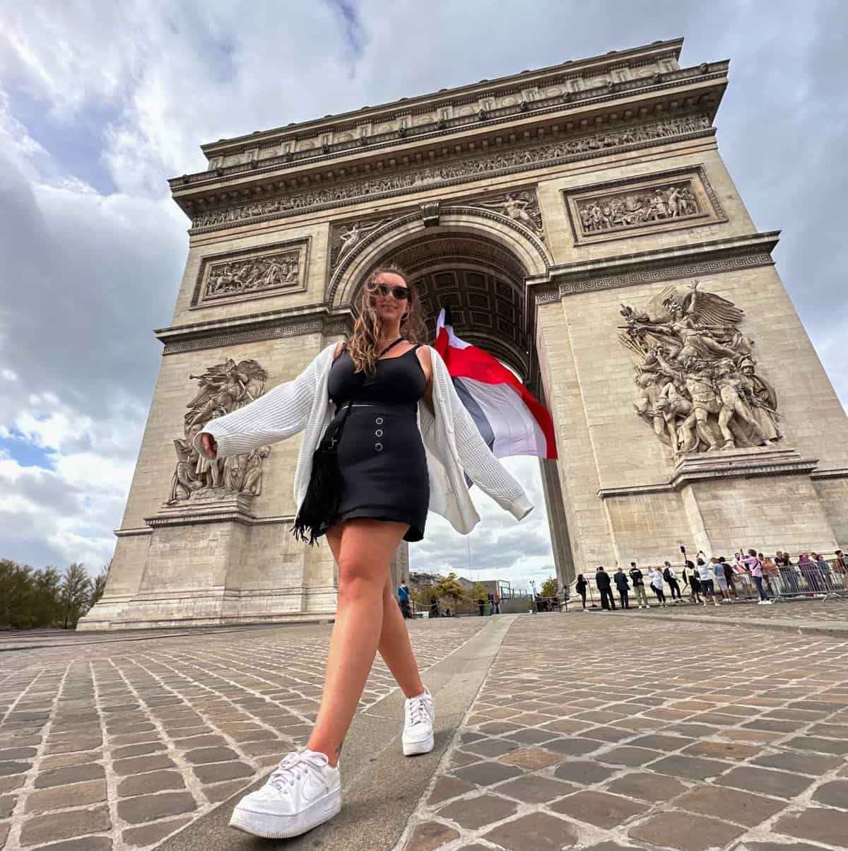 Jacqui walking towards the camera at a low angle in front of the Arc De Triomphe in Paris, France.