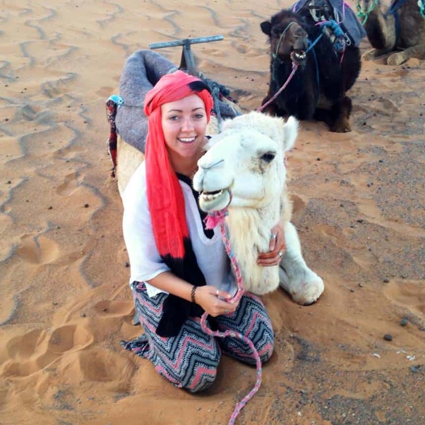 Me, a young woman traveler, posing with my camel in the sahara desert in Morocco.