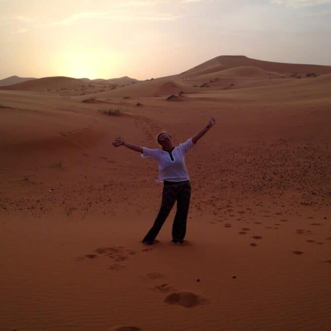 Jacqui, a young female traveler, posing in the vast Sahara Desert in morocco at sunset.